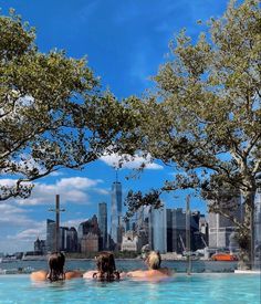 three people are sitting in the pool with their backs to each other and looking at the city