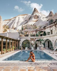 a woman sitting on the edge of a swimming pool in front of a mountain range