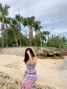 a woman sitting on the beach with her head in her hands and palm trees behind her