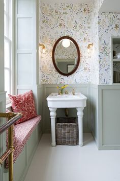 the bathroom is decorated in floral wallpaper and has a round mirror above the sink