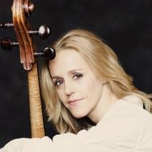 a woman with blonde hair holding a violin in her right hand and looking at the camera