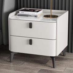 a white nightstand with two drawers and a book on top, next to a black chair