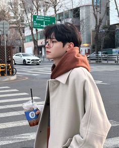 a young man standing on the side of a road holding a drink and looking off into the distance