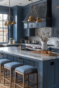 a large kitchen with blue cabinets and marble counter tops, gold pendant lights over the island