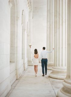 a man and woman are walking down the street in front of some white marble pillars