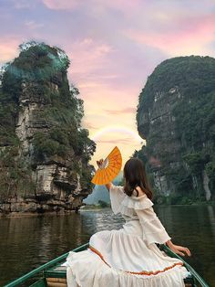 a woman in a white dress is sitting on a boat with an orange parasol