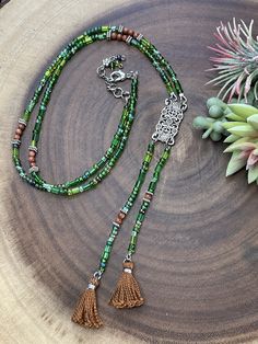 This gorgeous necklace with two tassels is designed with a unique look. It is made from a mix of czech glass beads in different shades of green and shapes. In between the purple beads are brown agate beads for a beautiful contrast. All metal components are silver plated. The pendant connector is vintage inspired rectangle shape that is about 1.25 inches long. The entire length of the pendant with tassels is 6.25 inches long. This necklace is similiar to a lariat style. The necklace length is 27.