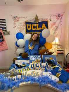 a woman sitting on top of a bed surrounded by blue and white balloons with the word ucla above her