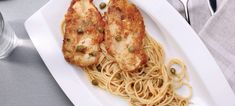 two pieces of chicken with noodles on a white plate next to silverware and forks