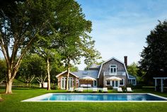 a house with a swimming pool in the front yard and lawn furniture around it, surrounded by trees