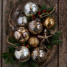 silver and gold christmas ornaments on a wooden plate with greenery in the center, top view from above