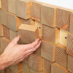 a person is placing wood blocks on top of each other to make a wall decoration