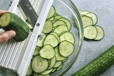 someone cutting cucumbers into slices in a bowl