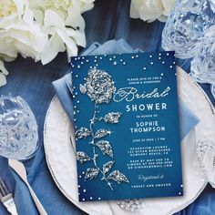 a blue and silver wedding shower is on a plate next to some glasses, napkins, and flowers