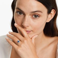 a woman wearing a ring with a blue stone on it's middle finger and her right hand near her face