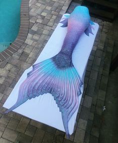 a large blue and purple mermaid tail on a white mat next to a swimming pool