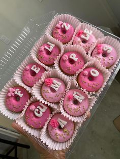 pink donuts with white frosting and sprinkles are arranged in a box