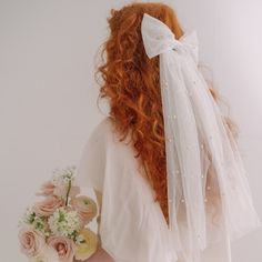 a woman with long red hair wearing a white veil and holding a bouquet of flowers