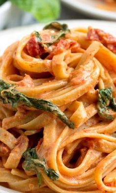 a white plate topped with pasta covered in tomato sauce and spinach garnish