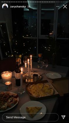 a table topped with pizza and candles in front of a window filled with lit candles