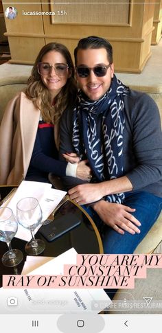 a man and woman sitting next to each other in front of a table with glasses on it