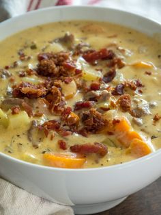 a white bowl filled with soup and meat on top of a wooden table next to a napkin