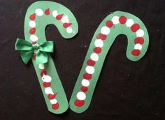 two paper candy canes with green bows on black tablecloth, one decorated in red and white polka dots