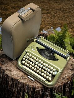 an old fashioned typewriter sitting on top of a tree stump next to a briefcase