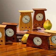 four wooden clocks sitting on top of a table next to pears and an apple