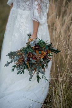 a woman in a white dress holding a bouquet of flowers and greenery on her wedding day