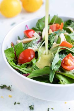 a salad in a bowl with dressing being poured into it and topped with fresh vegetables