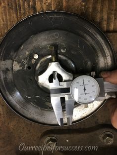 a person holding a wrench in front of a metal plate with a clock on it