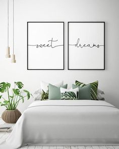 two framed posters on the wall above a bed with pillows and plants in vases