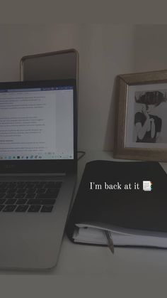 an open laptop computer sitting on top of a desk next to a book and framed photograph