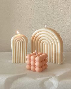 an assortment of candles on a table with white sheets and wall in the back ground