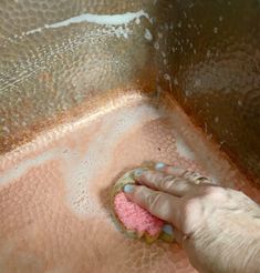 a person with a sponge on their hand cleaning a metal sink drain in the bathroom