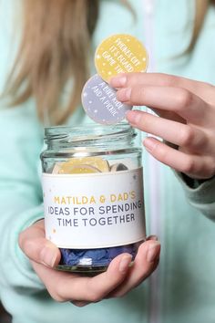 a woman holding a jar filled with lots of things to put in her hand and some stickers on it