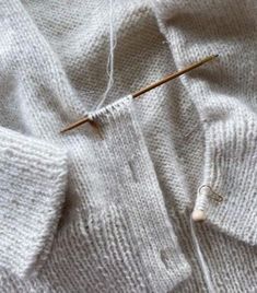 a pair of knitting needles sitting on top of a white knitted sweater with buttons