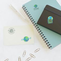 a notepad, pen and paper clips on top of a notebook with the word earth printed on it