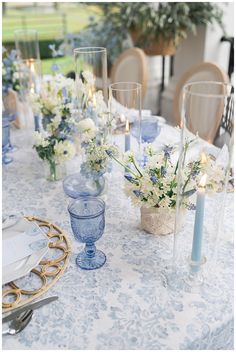 the table is set with blue and white floral centerpieces, candles, and glass vases