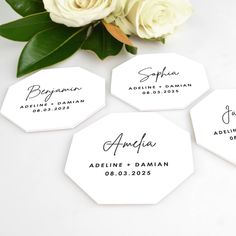 three white roses are sitting next to four hexagonal tags with names on them