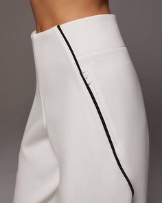 a woman in white pants with black zippers on the side and her right leg