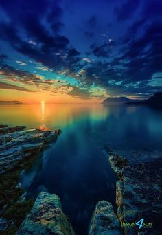 the sun is setting over water with rocks in front of it and an ocean view