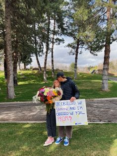 a man and woman standing next to each other in the grass holding a sign that says,