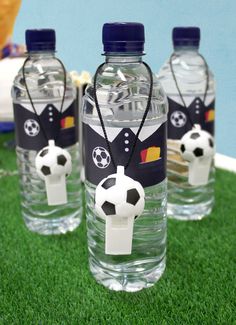 three plastic water bottles with soccer themed labels on them sitting on green grass next to a blue wall