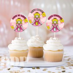 three cupcakes with white frosting and pink decorations