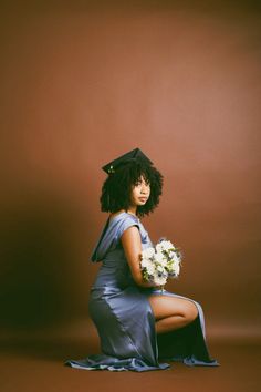 a woman in a graduation cap and gown sitting on the ground with flowers around her legs