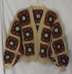 a crocheted sweater hanging on a clothes hanger in front of a white backdrop