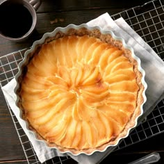 an apple pie sitting on top of a cooling rack next to a cup of coffee