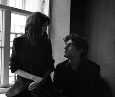 a man and woman sitting next to each other near a window in black and white